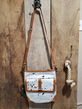 Hide crossbody bag with brown accents hanging on a wooden wall.